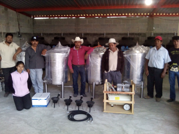 Six men and one woman next to large metal vats and equipment for brewing fertilizer